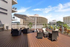 A rooftop deck with outdoor furniture and a view of a curved building in the background. - 79 Harbour Lights with Parkland & Marina Views (Cairns City)