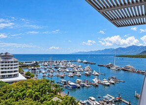 A marina with numerous boats docked, surrounded by lush greenery and mountains in the background. - 79 Harbour Lights with Parkland & Marina Views (Cairns City)