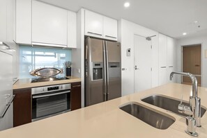 Une cuisine moderne dotée d’appareils électroménagers en acier inoxydable, d’un évier à deux bacs et de meubles blancs.