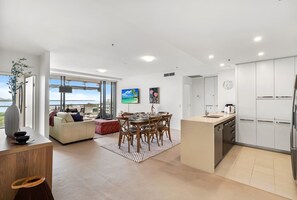 A modern living space with a dining area, kitchen, and large windows offering a view. - 79 Harbour Lights with Parkland & Marina Views (Cairns City)