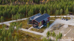A modern building with a glass facade and a red exterior, surrounded by a forested area. - Levi North Apartment D4 by Aavalevi (Levi)