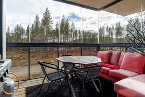 A room with a large window overlooking a forest, a table with chairs, and a red sofa. - Levi North Apartment D4 by Aavalevi (Levi)