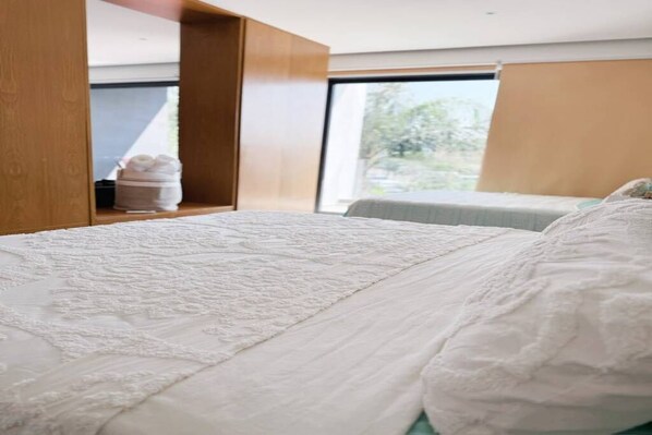 Una camera d'albergo moderna con un letto grande, una testiera in legno, una finestra vista e un piccolo ripiano con asciugamani.