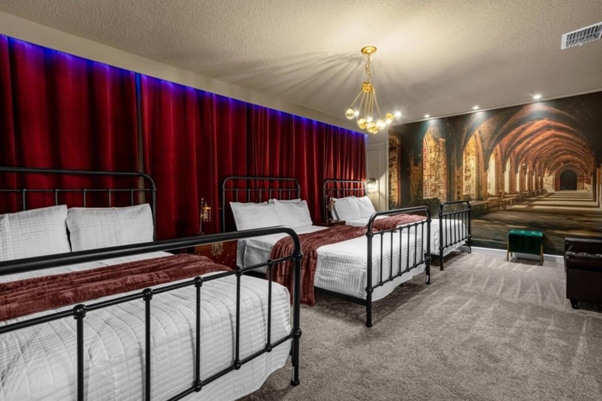 A hotel room with three beds, red curtains, a chandelier, and a mural of a cathedral.