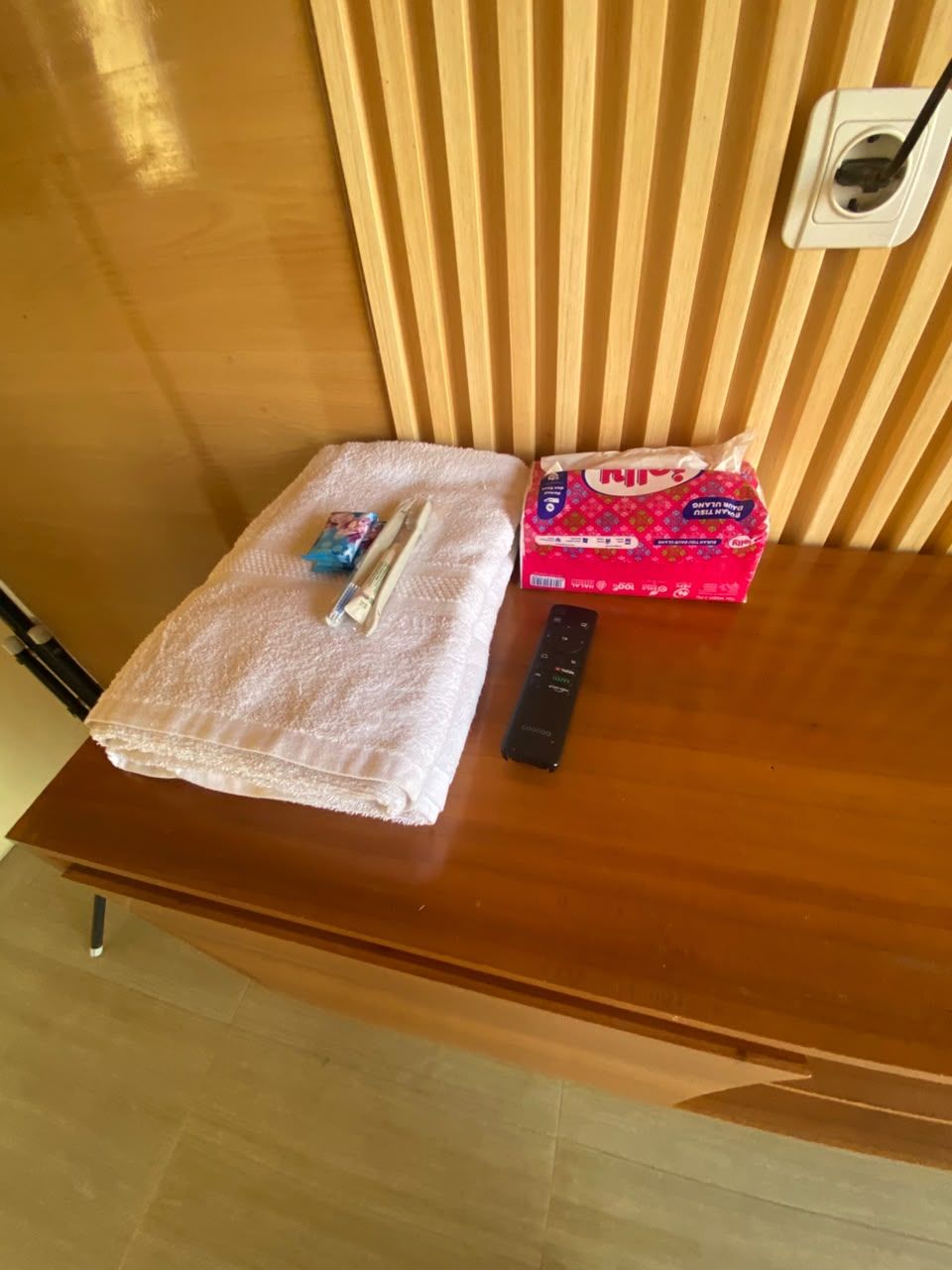 A wooden table with a folded towel, a remote control, and a tissue box.