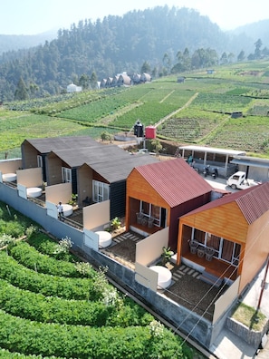 A modern hotel with multiple rooms, a covered outdoor area, and a view of surrounding green fields and hills. - Lawu View Glamping (Karanganyar)