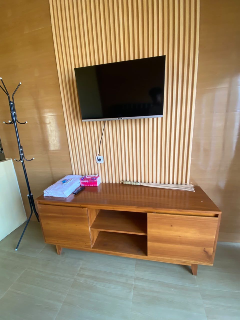 Un meuble de rangement en bois pour appareils multimédias, avec un téléviseur à écran plat, une boîte rose et une télécommande.