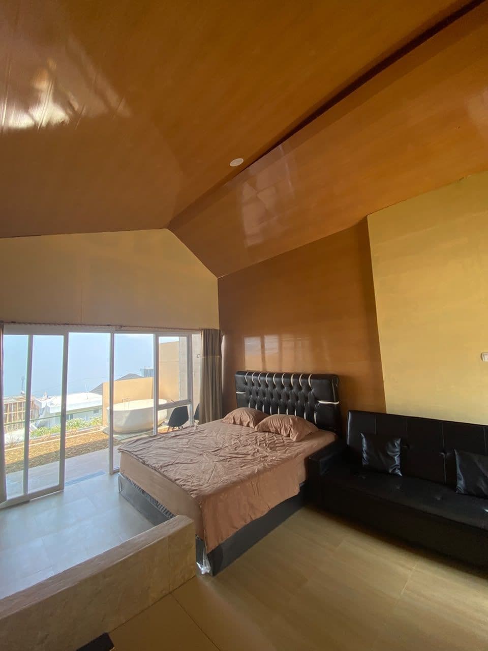 A modern bedroom with a large bed, a sofa, and a balcony with a view.