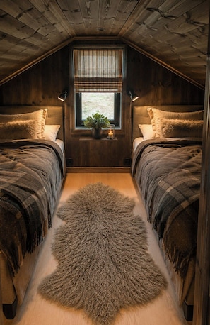 A cozy attic bedroom with two beds, a large fur rug, a window with curtains, and a small plant on the windowsill. - Family cabin by the ski trails on Sjusjøen (Sjusjøen)