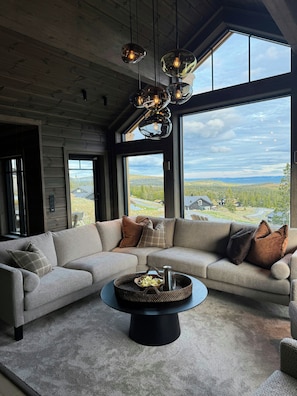 A modern living room with a sectional sofa, a coffee table, and a view of a landscape through large windows. - Family cabin by the ski trails on Sjusjøen (Sjusjøen)