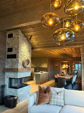 A cozy cabin interior with a stone fireplace, wooden ceiling, and a dining area with a view. - Family cabin by the ski trails on Sjusjøen (Sjusjøen)