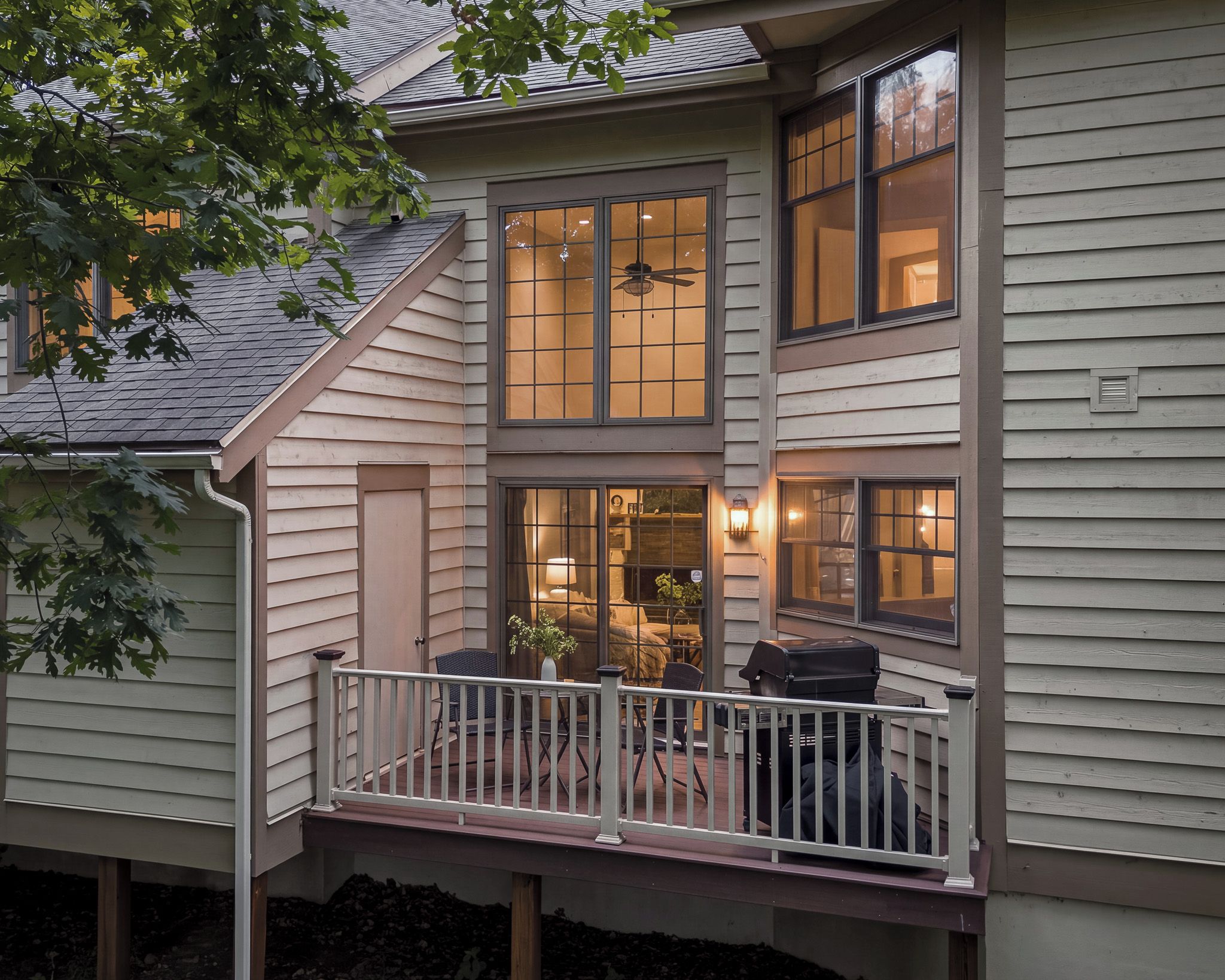A two-story house with a balcony, large windows, and a visible interior with a ceiling fan.