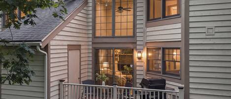 A two-story house with a balcony, large windows, and a visible interior with a ceiling fan.