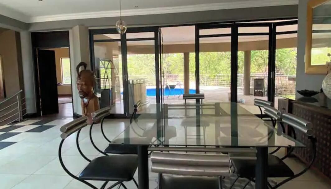 A dining area with a glass table and chairs, a view of the outdoors, and a staircase leading to another level.