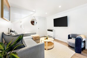 Uma sala de estar moderna com um sofá cinzento, uma mesa de centro redonda e uma televisão de tela plana fixada na parede.