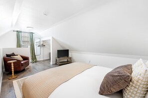 Een slaapkamer met een bed, een televisie op een standaard, een bank en een raam met gordijnen.