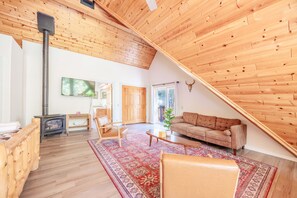 A spacious living area with a high ceiling, wooden walls, a sofa, a coffee table, a rug, and a fireplace. - New! Bearadise ~ Timberlodge Mountain Retreat (Big Bear Lake)