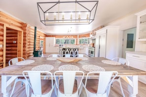 Interior de uma cabana de madeira com uma mesa de jantar, cadeiras, um lustre e uma cozinha.