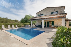 Una casa a due piani con piscina, area relax esterna e facciata in pietra.