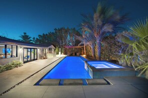 Een modern huis met een zwembad, een overdekt terras en een goed verlicht buitengebied.