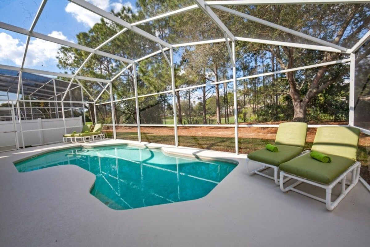 A covered swimming pool with lounge chairs and a view of trees.