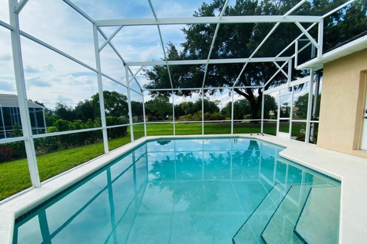 A clear swimming pool with a glass enclosure, surrounded by a white fence, and a building adjacent to it.