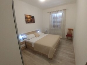 A hotel room with a bed, bedside table, chair, and a window with curtains. - Four Bedroom Holiday Home With Terrace & Sea View (Jelsa)