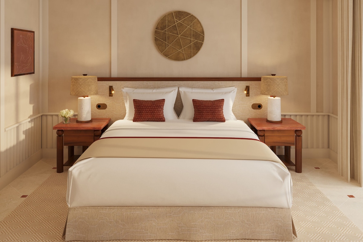 A hotel room with a large bed, two bedside tables, a round wall decoration, and a framed picture on the wall.