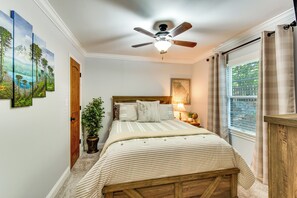 Une chambre à coucher avec un lit, un ventilateur de plafond, une fenêtre avec des rideaux et des œuvres d’art murales.