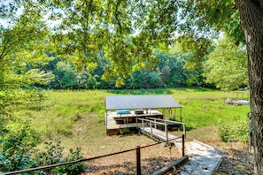 Une terrasse en bois surmontée d’un toit en métal, entourée d’une pelouse et d’arbres.