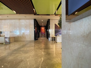 Een hotel lobby met een marmeren vloer, een receptiebalie en een groene accentmuur.