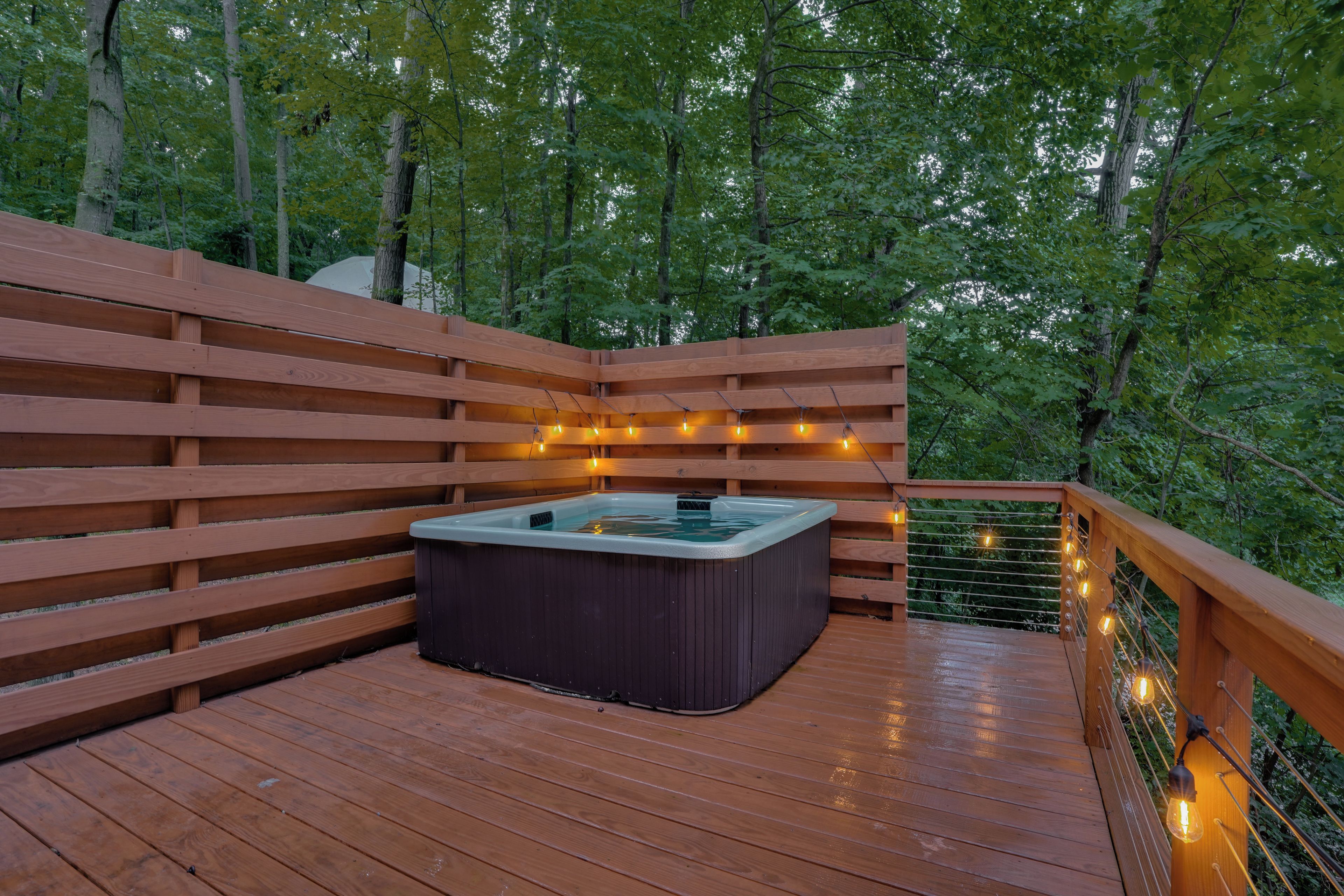 A wooden deck with a hot tub and string lights.