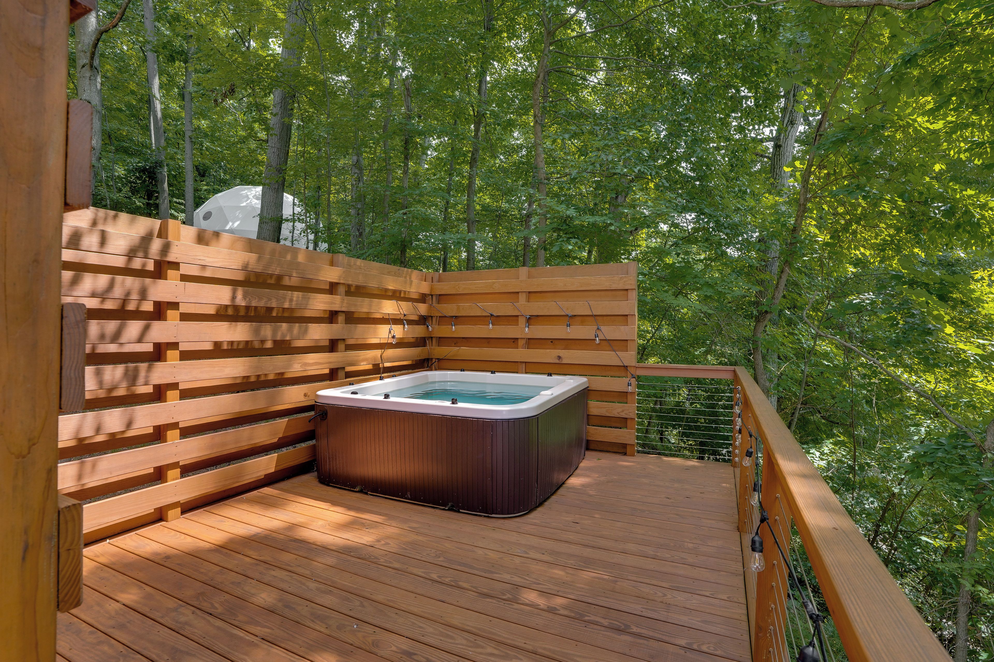 Ein Whirlpool auf einer Holzterrasse, umgeben von Bäumen.