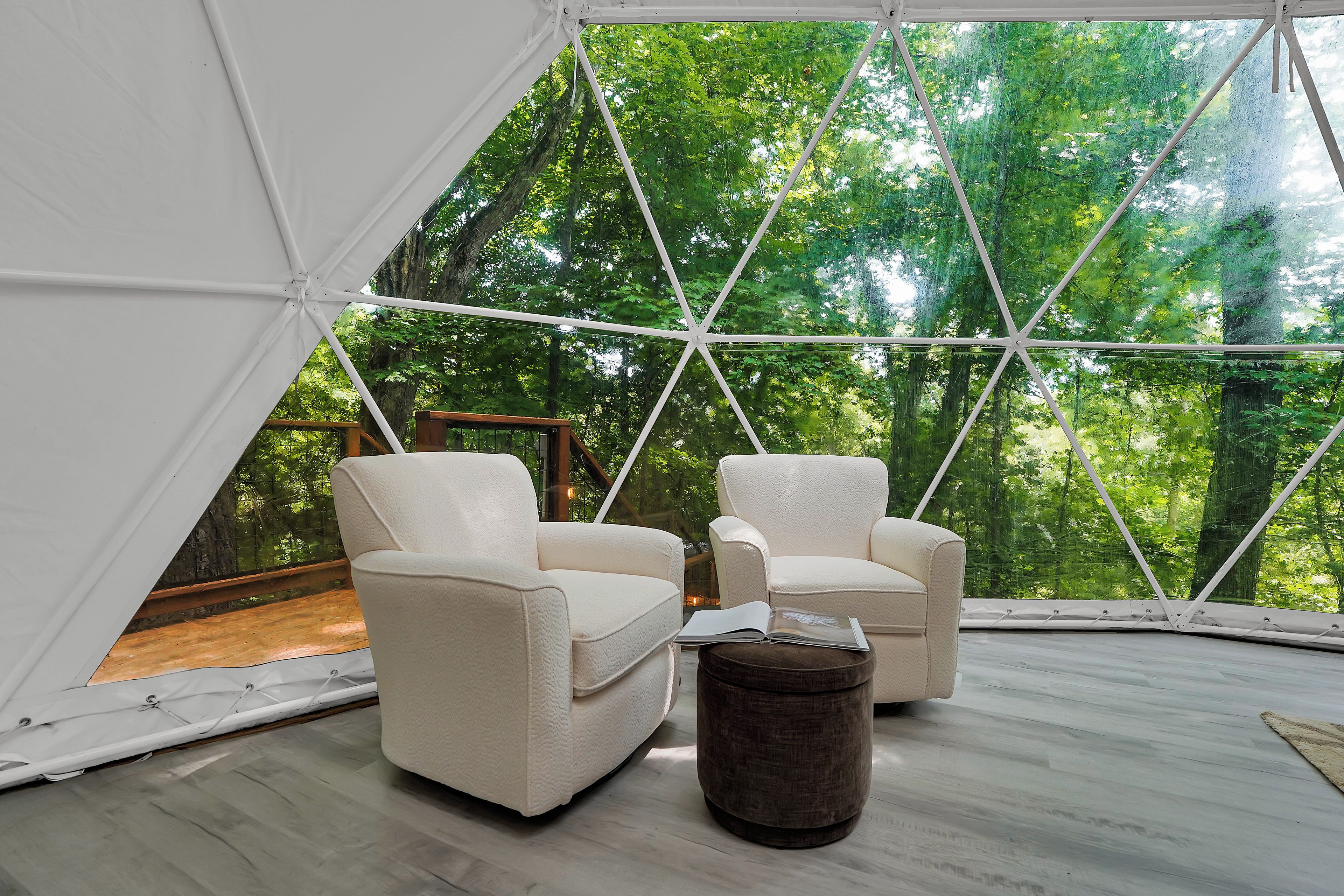 Una habitación con tienda de campaña, dos sillones blancos y un otoman marrón.