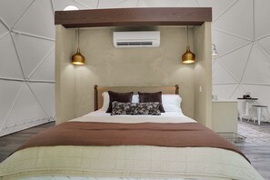 Un dormitorio moderno con cama, dos lámparas colgantes, un equipo de aire acondicionado y una pequeña mesa con una silla.
