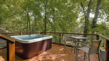 Een hottub op een houten terras met een tafel en stoelen, omgeven door een metalen reling en bomen.