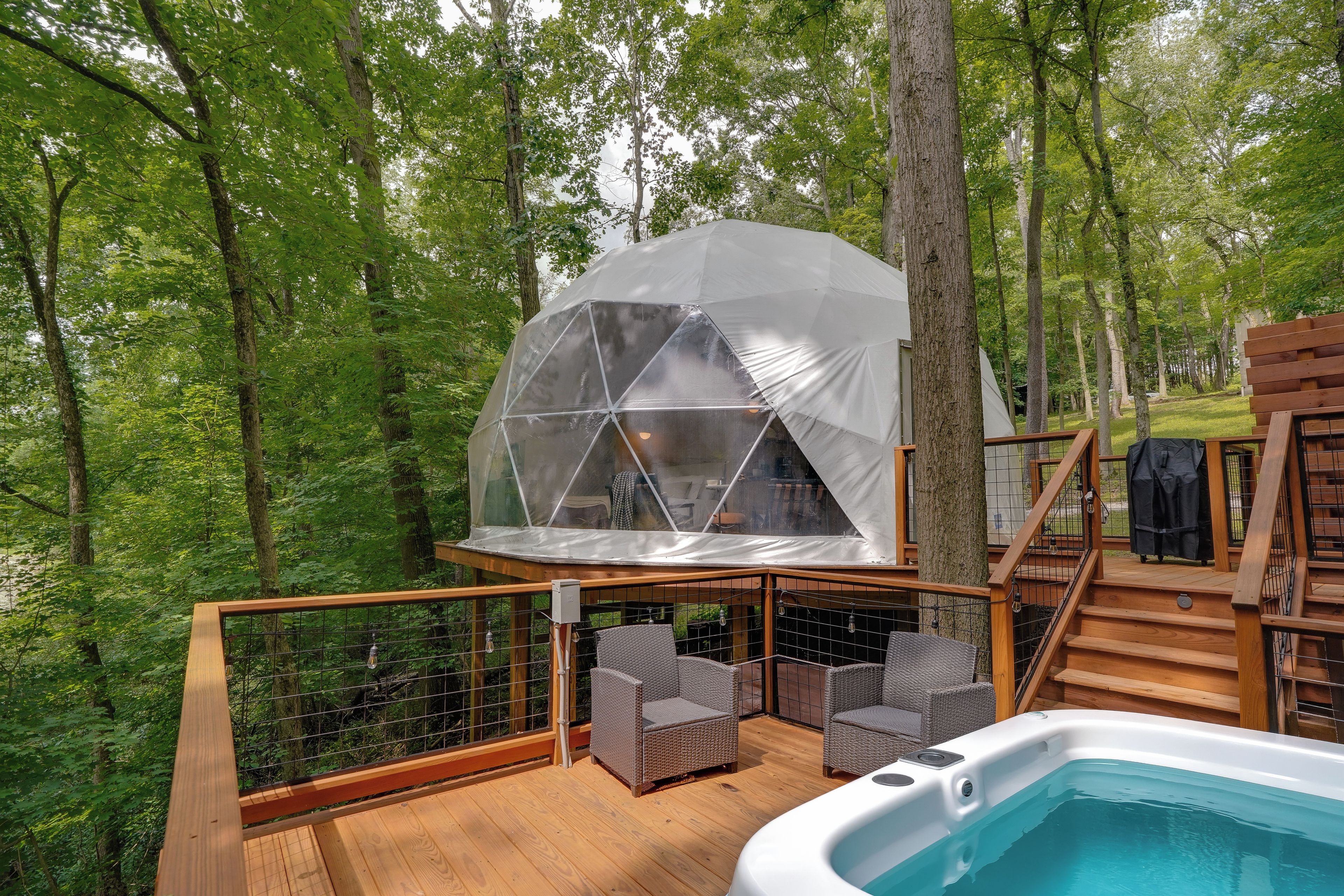 Eine Holzterrasse mit Whirlpool, Korbstühlen und einer geodätischen Kuppelstruktur.