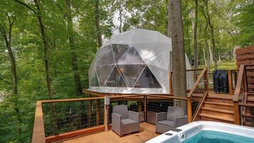 Eine Holzterrasse mit Whirlpool, Korbstühlen und einer geodätischen Kuppelstruktur.