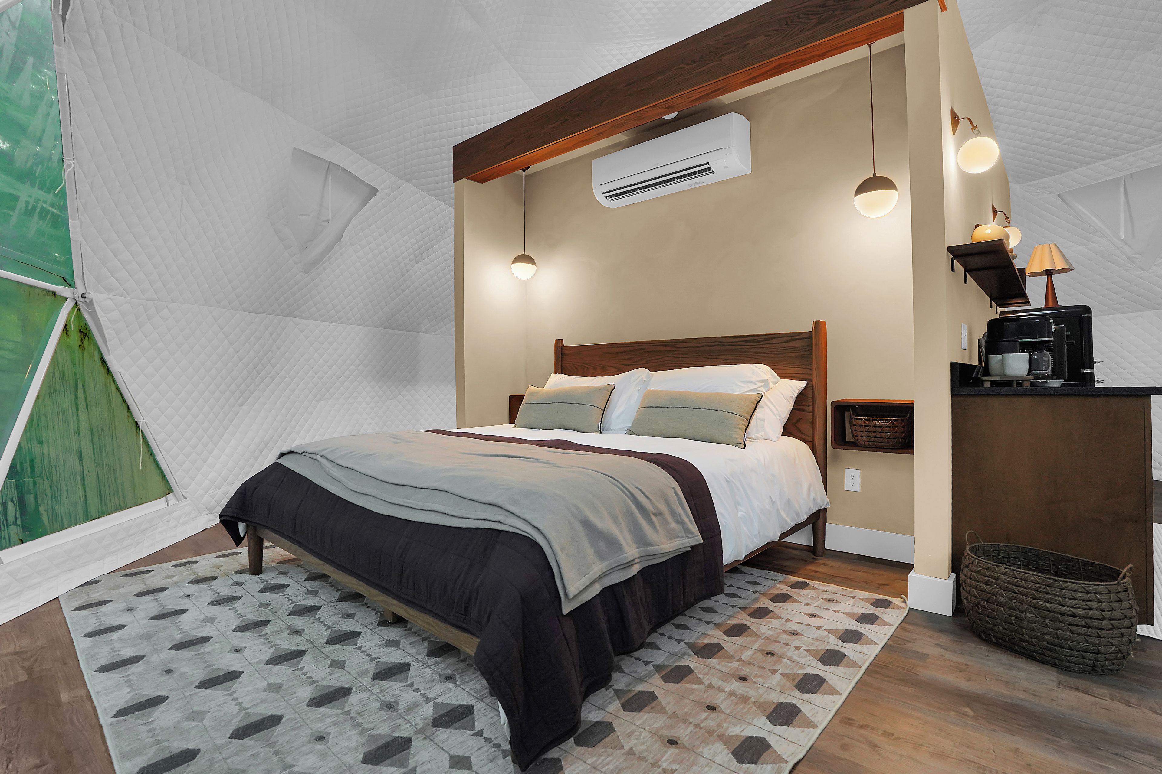 Ein Schlafzimmer mit einem Bett, Nachttischen, einer Klimaanlage, einer Lampe und einem kleinen Regal mit einer Kaffeemaschine.