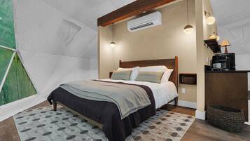 Ein Schlafzimmer mit einem Bett, Nachttischen, einer Klimaanlage, einer Lampe und einem kleinen Regal mit einer Kaffeemaschine.