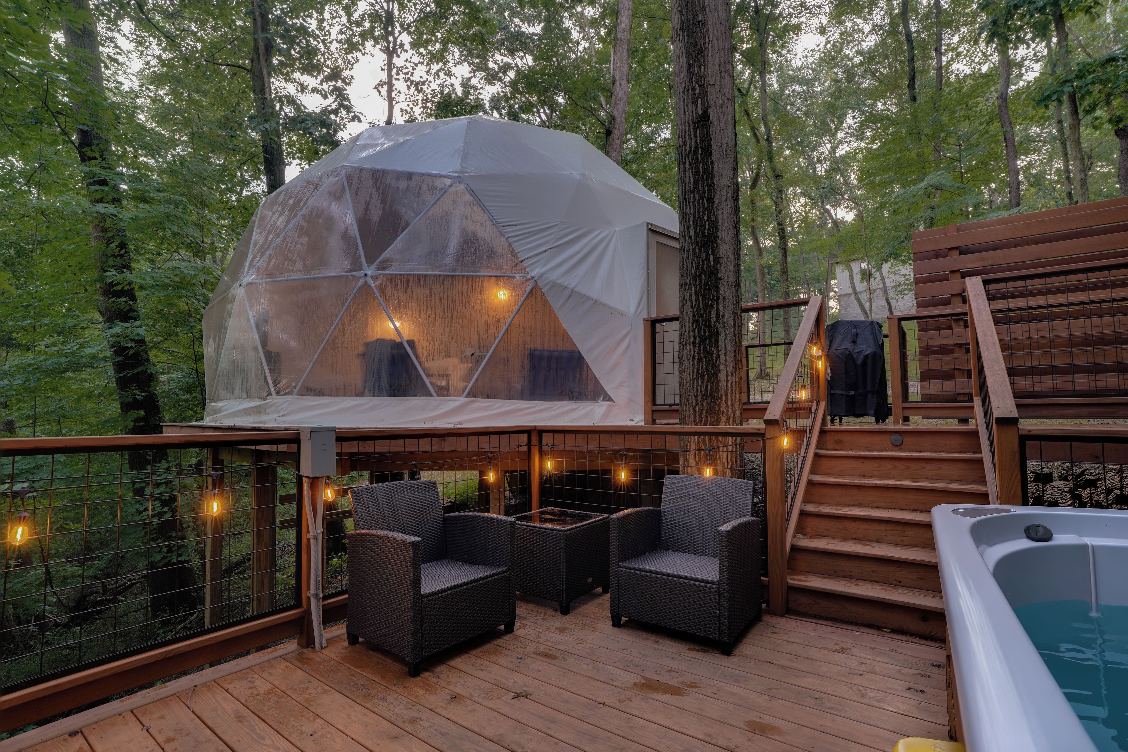 Ein kuppelförmiges Zelt mit Blick auf den Wald, eine Holzterrasse mit Stühlen und eine Whirlpool.