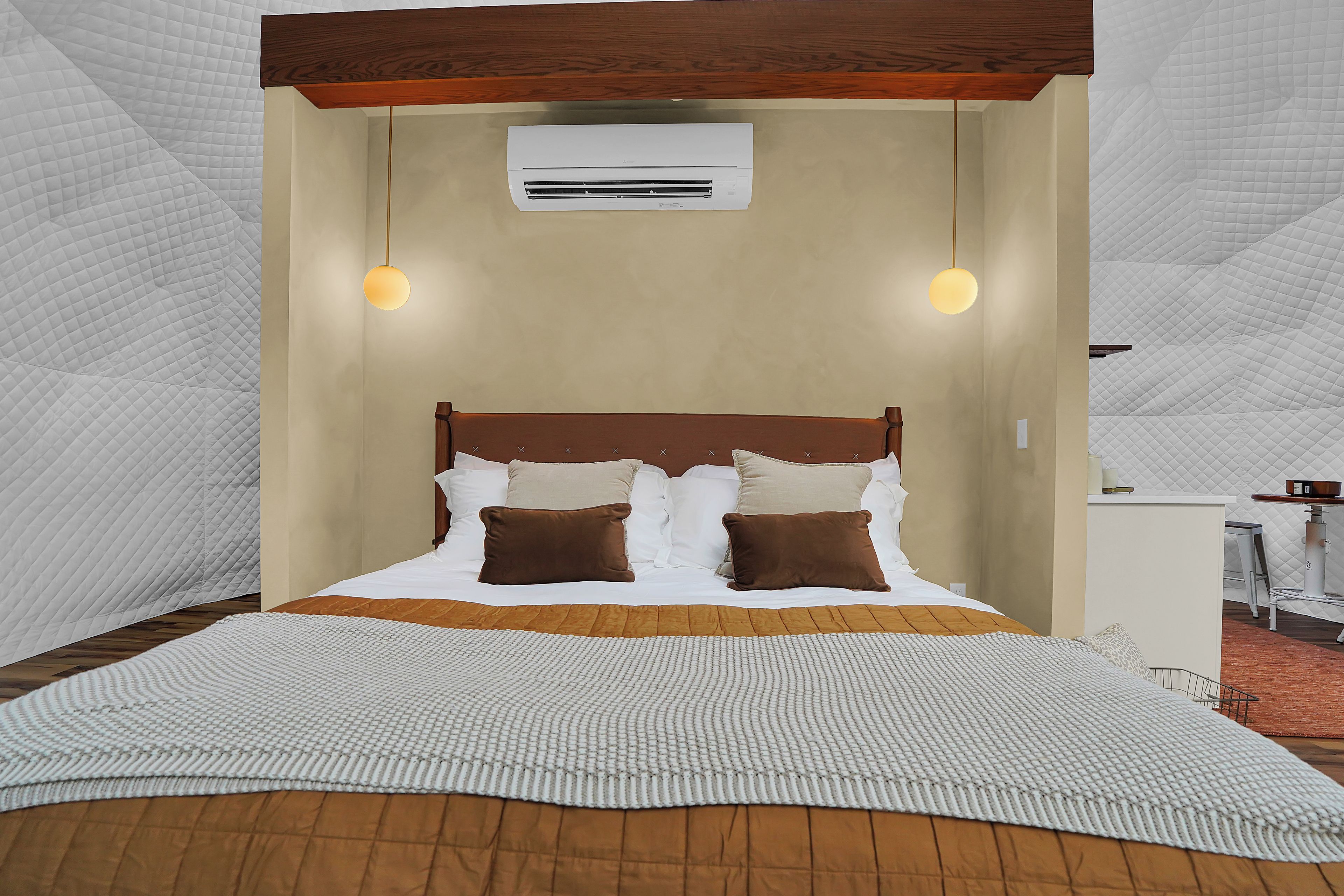 A bed with a wooden headboard, two bedside lamps, and a wall-mounted air conditioner.