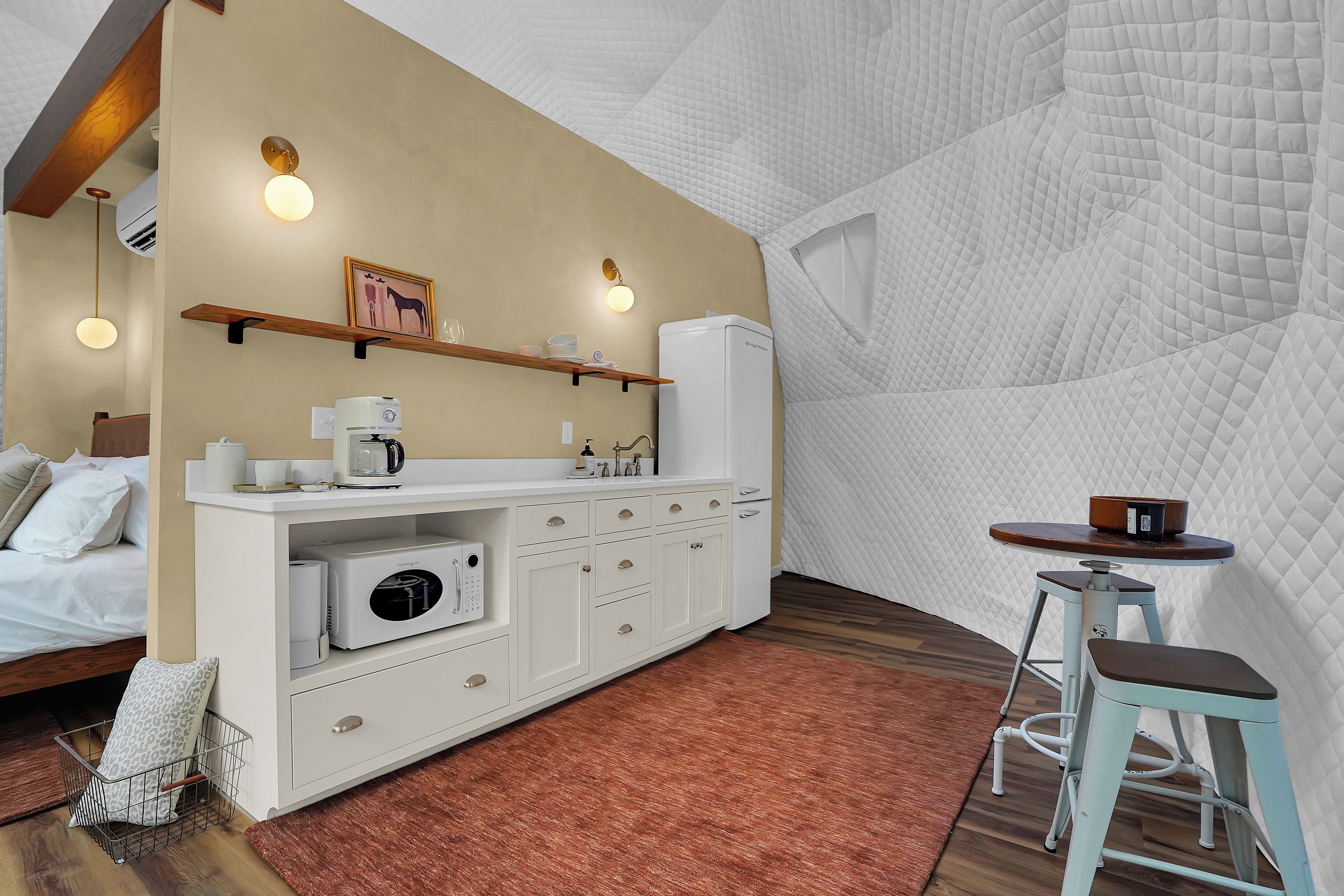 Habitación de hotel compacta con kitchenette, una cama, una pequeña mesa y un taburete.