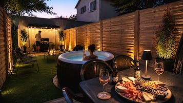 Eine Terrasse im Freien mit Whirlpool, Esstisch gedeckt mit Speisen und Getränken, und eine Person, die im Hintergrund entspannt.