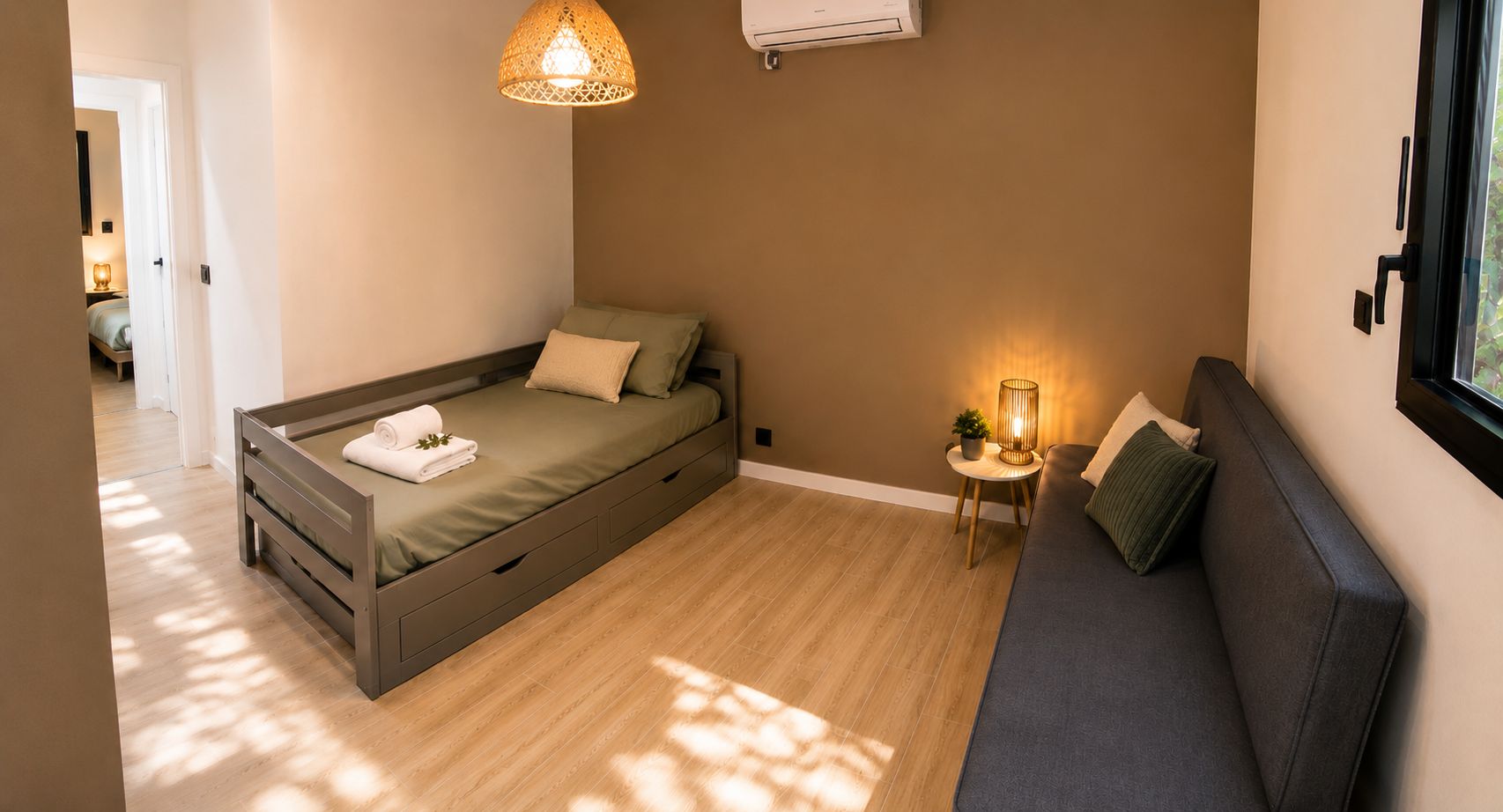 Une chambre à coucher de taille réduite, comprenant un lit, un canapé, une petite table avec une lampe et un appareil de climatisation.