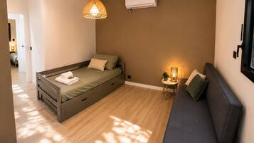 Une chambre à coucher de taille réduite, comprenant un lit, un canapé, une petite table avec une lampe et un appareil de climatisation.