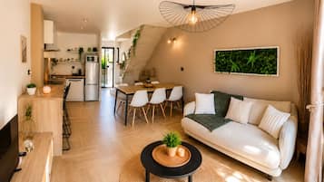 A modern living space with a dining area, a sofa, and a kitchen in the background.