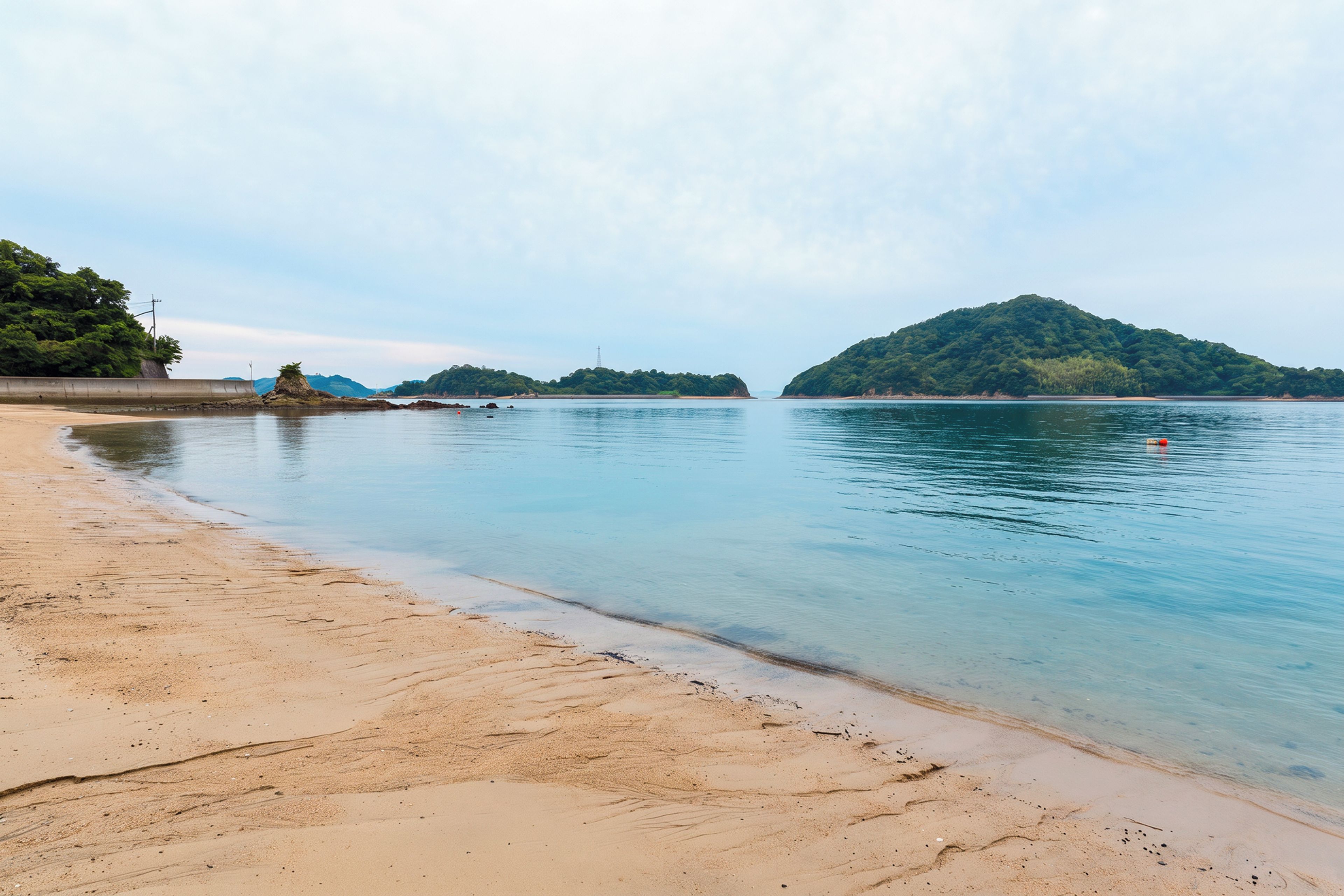 A beach with clear water, a sandy shore, and a forested island in the distance.