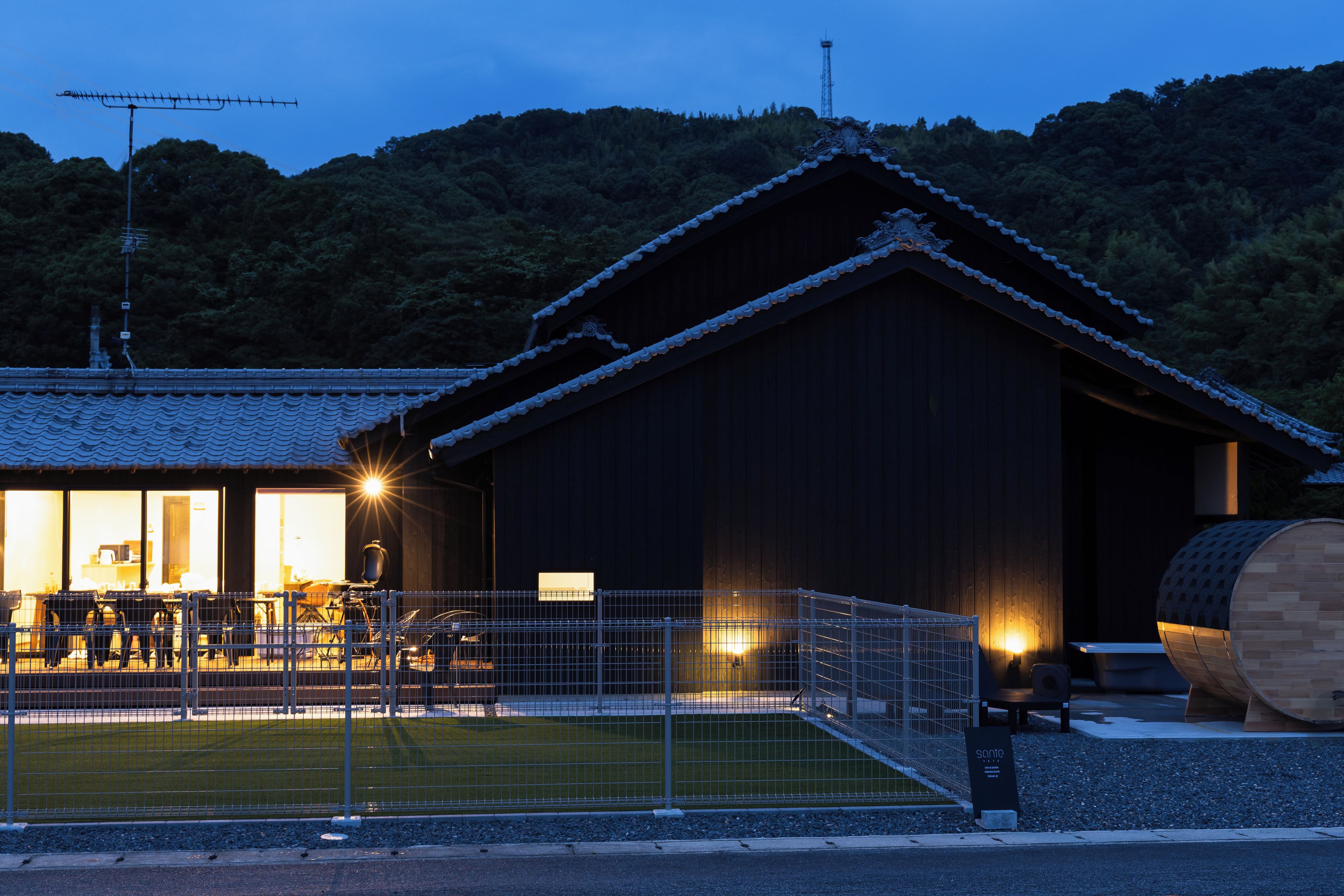 A building with a traditional roof, a fenced area with seating, and a signboard.