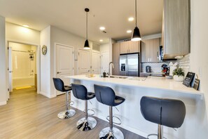 A modern kitchen with a central island, bar stools, stainless steel appliances, and pendant lighting. - 2BR Coastal Condo in Bradenton | 3 Mi to IMG (Bradenton)